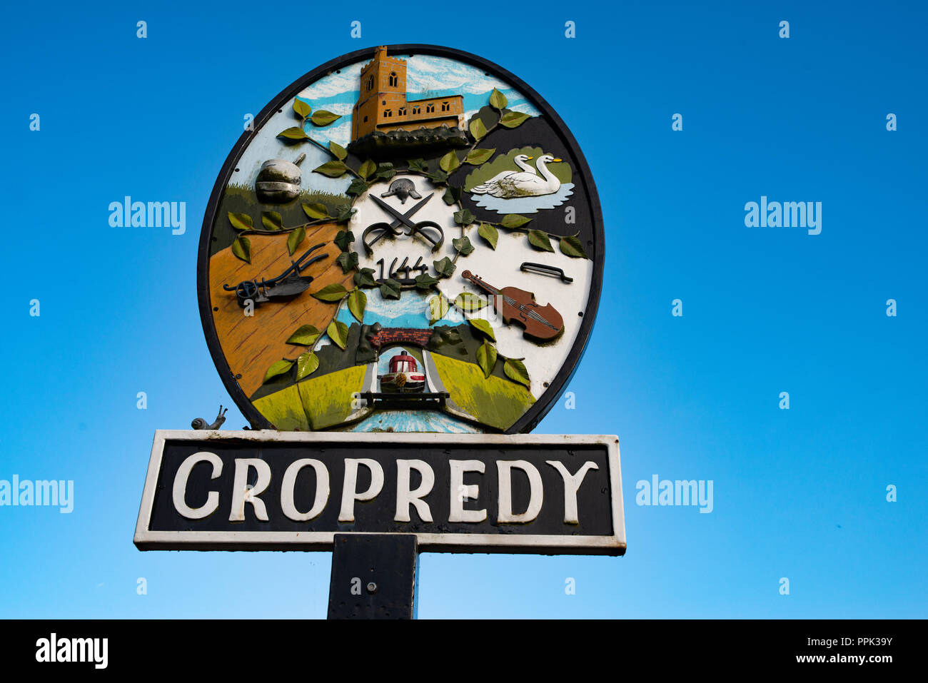 Traditional village brightly colourful round metal sign for Cropredy against a clear blue sky. Stock Photo