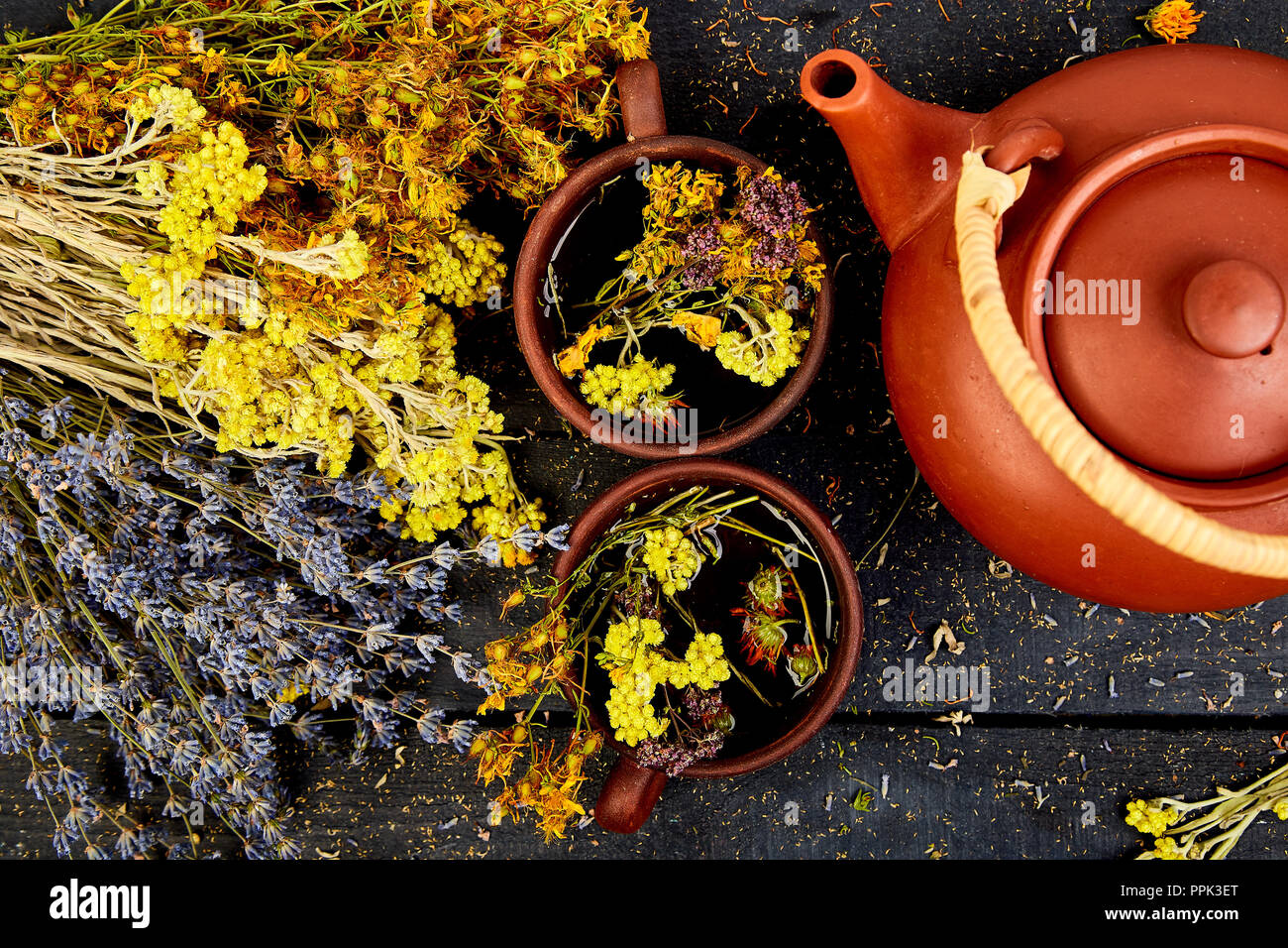 Two  Cup of herbal tea - tutsan, sagebrush, oregano, helichrysum, lavender near brown teapot on dark wooden background. Herbal tea. Dry Herbs and flow Stock Photo
