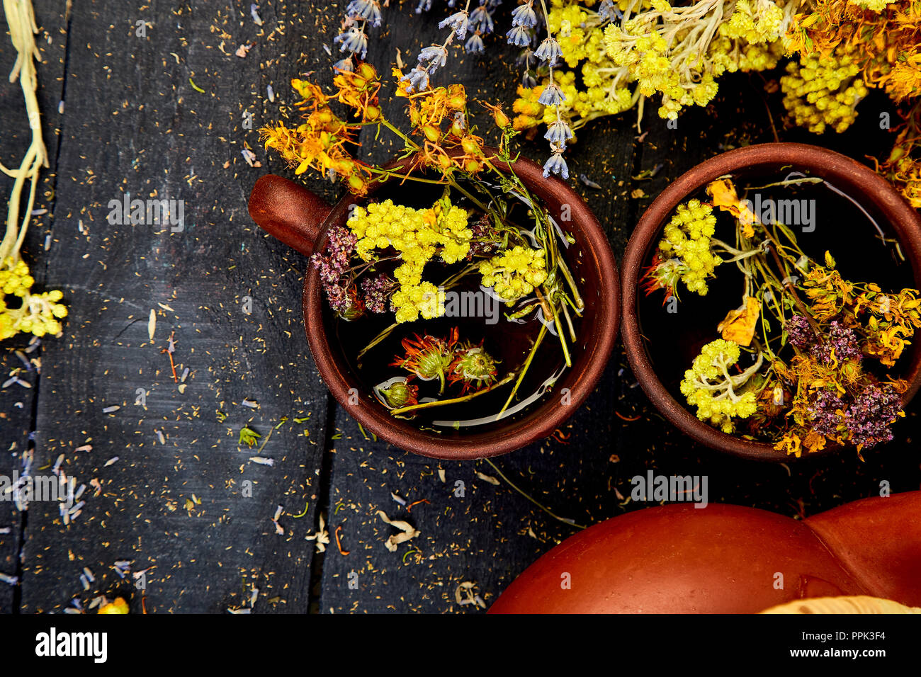 Two  Cup of herbal tea - tutsan, sagebrush, oregano, helichrysum, lavender near brown teapot on dark wooden background. Herbal tea. Dry Herbs and flow Stock Photo