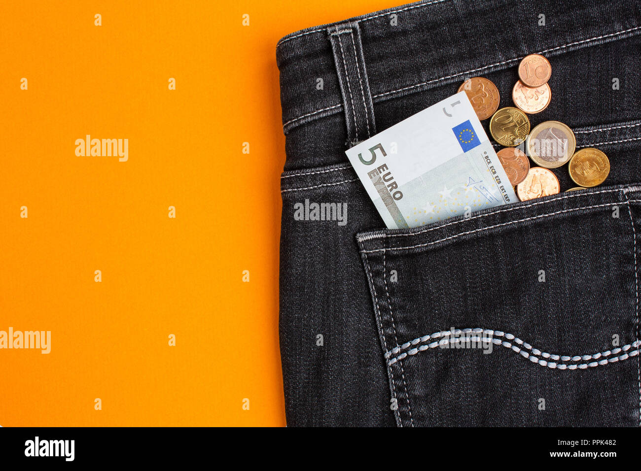 Euro banknote and coins in black jeans back pocket on orange background Stock Photo