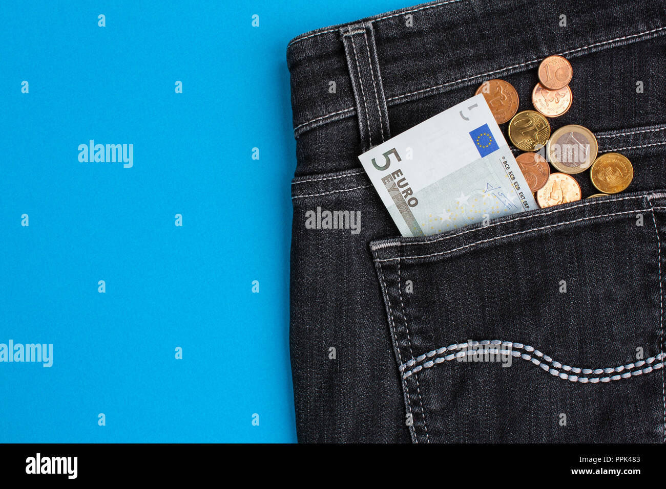Euro banknote and coins in black jeans back pocket on blue background Stock Photo