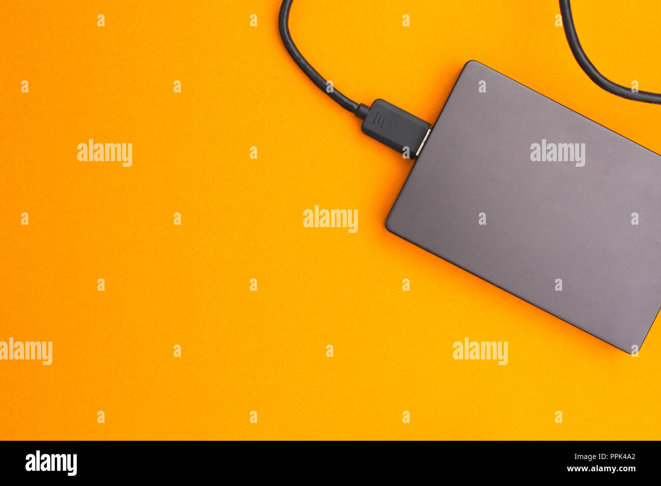 Black external hard disk with USB cable on orange background. Top view. Stock Photo