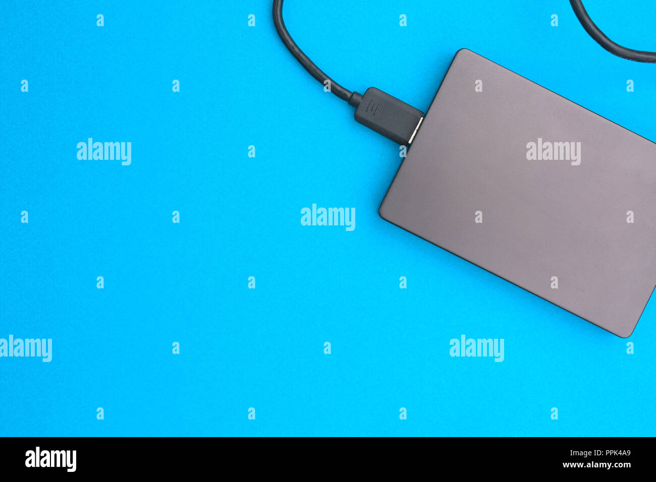 Black external hard disk with USB cable on blue background. Top view. Stock Photo