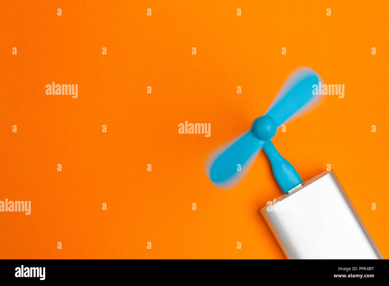 A blue usb fan is inserted into the  a silver pot of power and spinning on an orange background with copy space Stock Photo