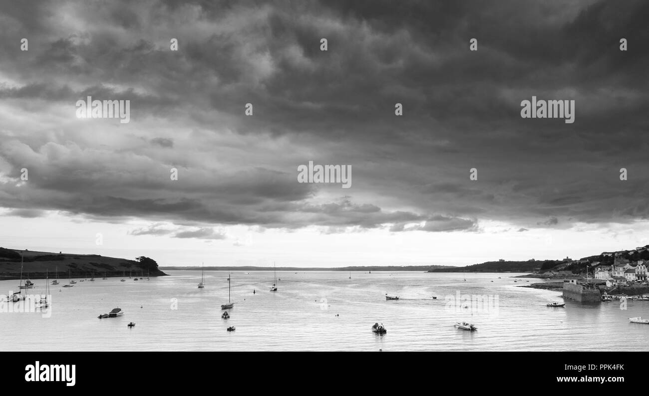 Black and white view of heavy stormy clouds over the sea and harbour of St Makes with small boats in the foreground. Stock Photo