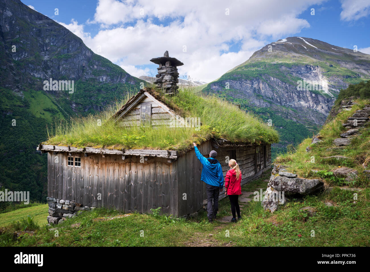 Kagefla - mountain farms on the mountainsides along the Geirangerfjorden fjord. Tourist attraction of Norway. A pair of travelers visiting traditional Stock Photo