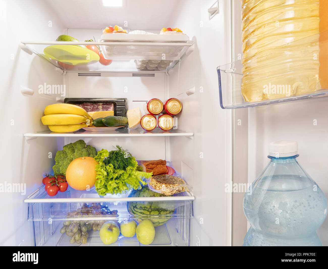 Fresh food and drink in the open and illuminated fridge. Stock Photo