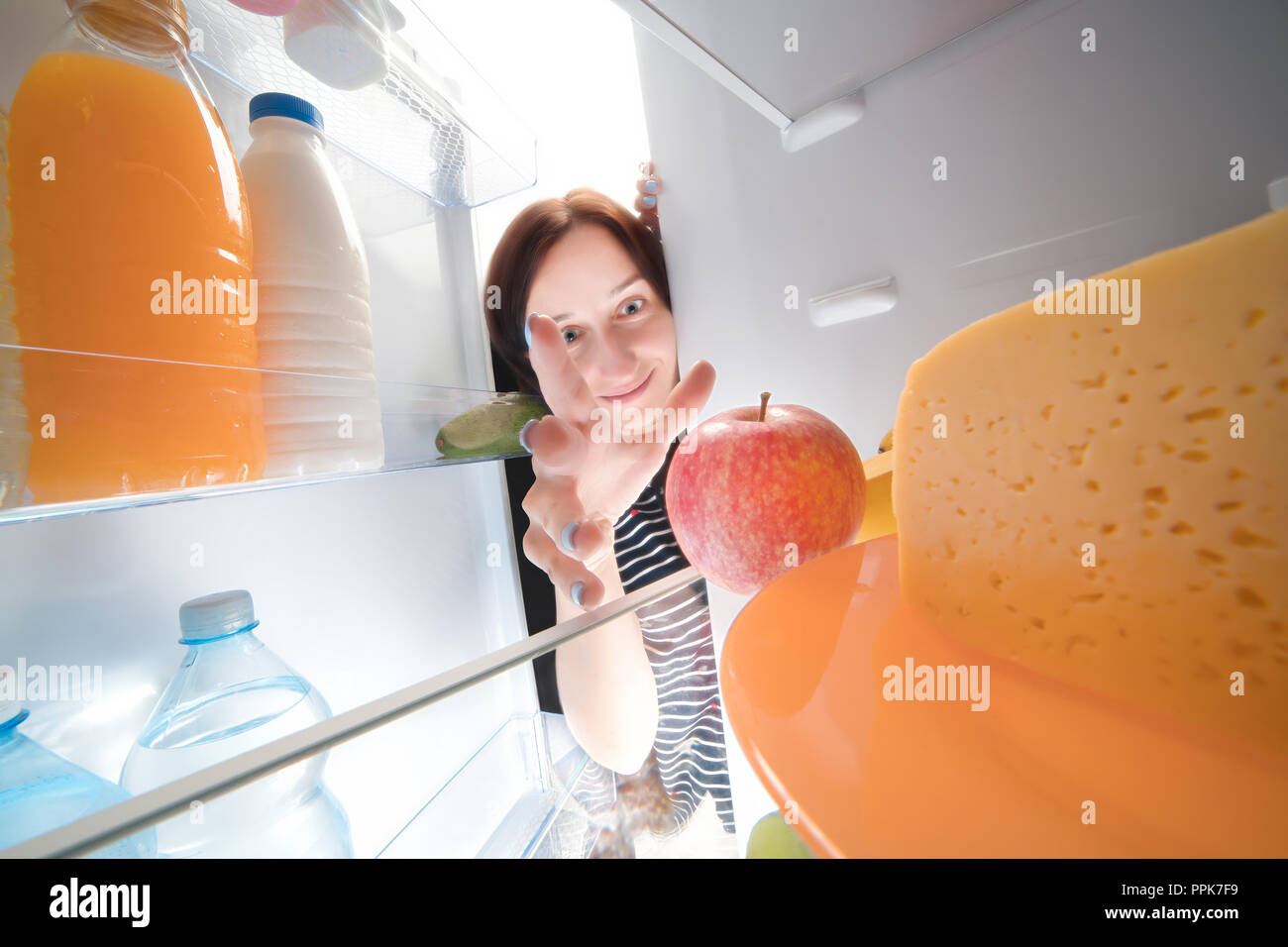 Funny happy girl taking apple from the fridge. View from inside Stock Photo