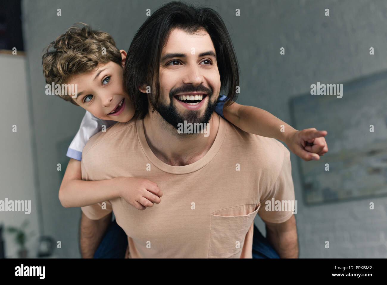 portrait of happy father and little son pointing away while piggybacking together at home Stock Photo