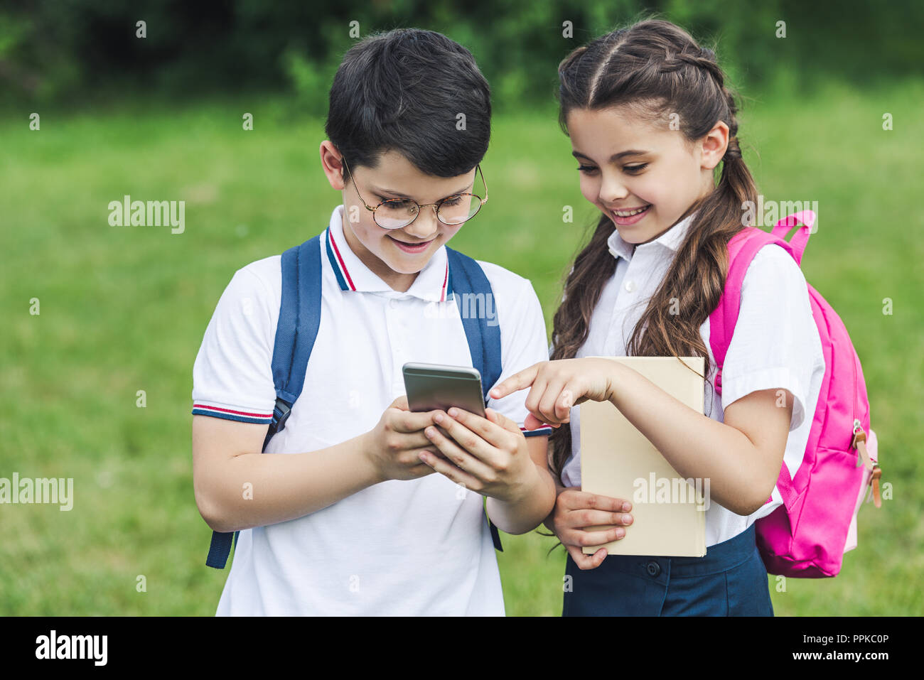 adorable schoolchildren using smartphone outdoors together Stock Photo