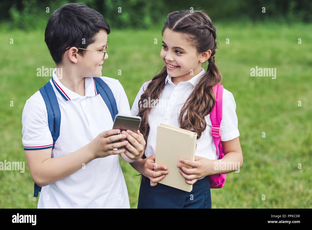 smiling schoolchildren using smartphone outdoors together Stock Photo