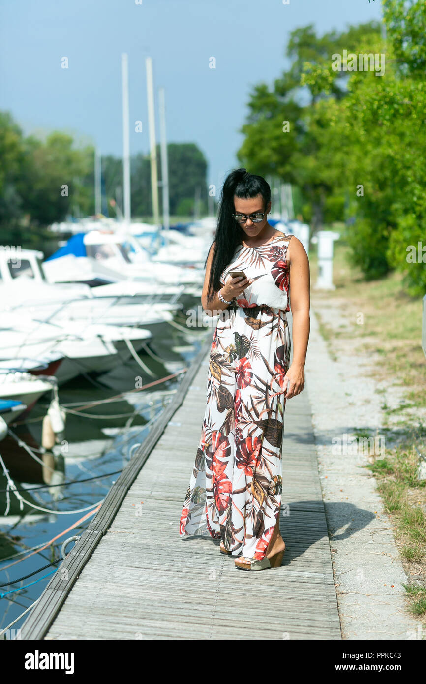 Stylish young woman with smartphone in hands on the pier. Communication and roaming during the holidays and travel. Concept Summer Holidays Stock Photo