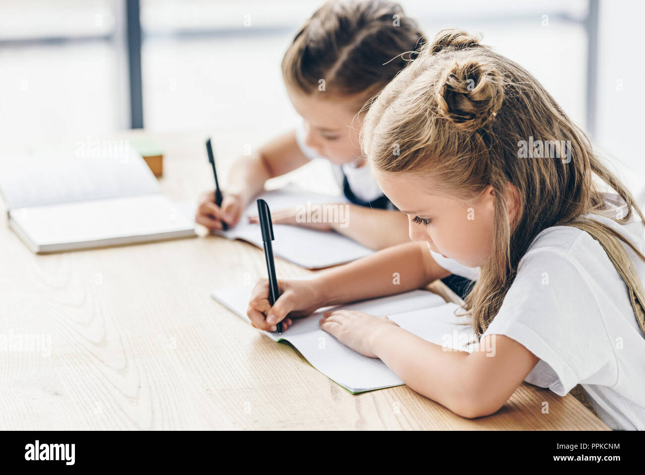 little schoolgirls writing in notebooks while doing homework isolated ...