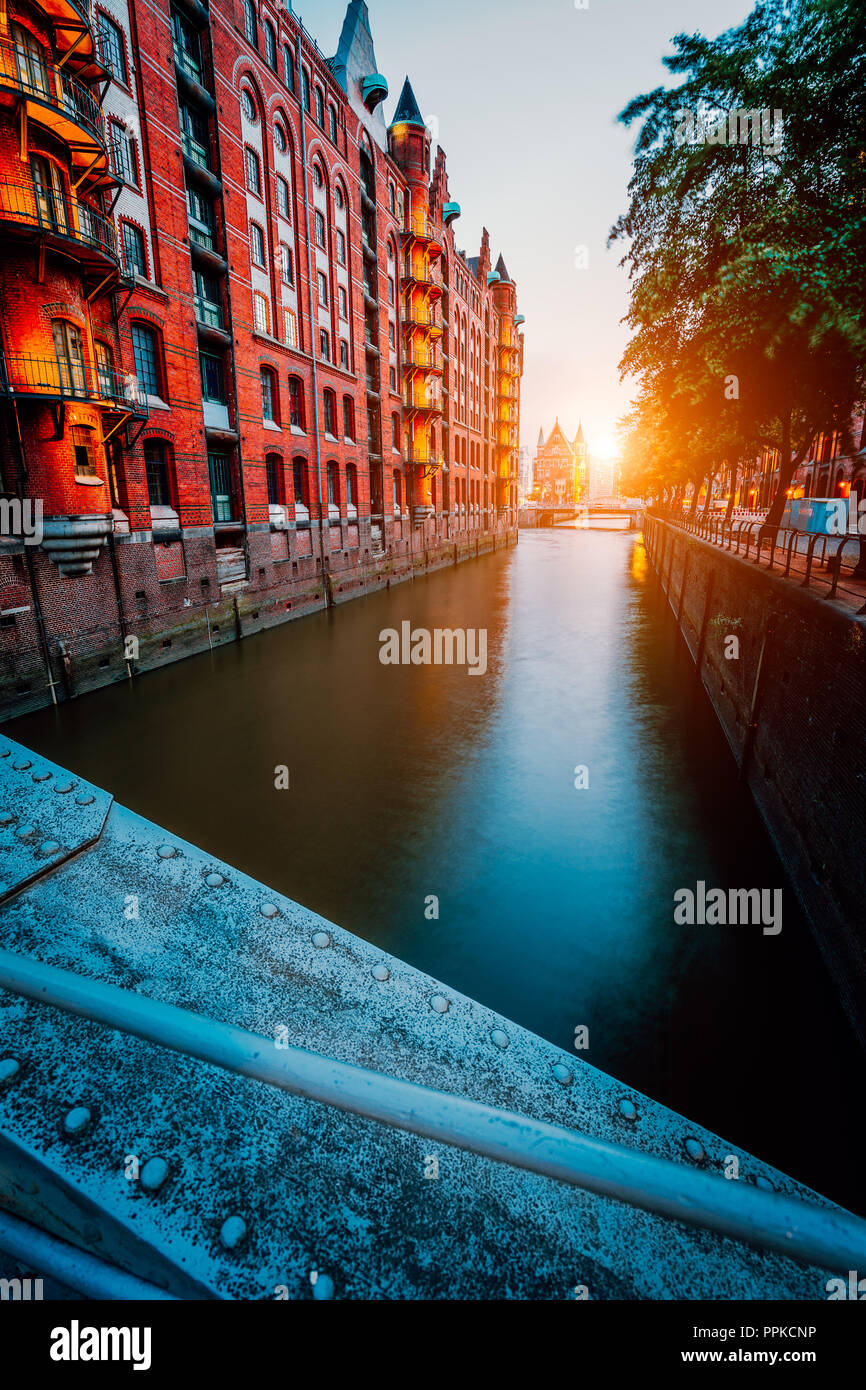 Touristic spot old red brick illuminated buildings, canal and square in golden sunset light. Speicherstadt Hamburg. Warehause District at dawn Stock Photo
