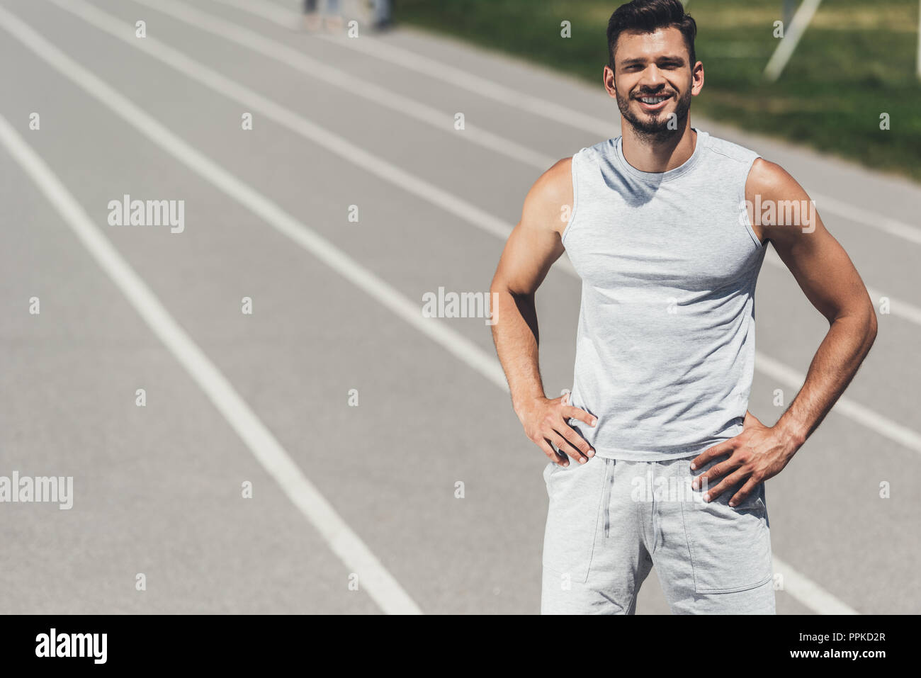 smiling young sporty man standing on running track with arms akimbo Stock Photo