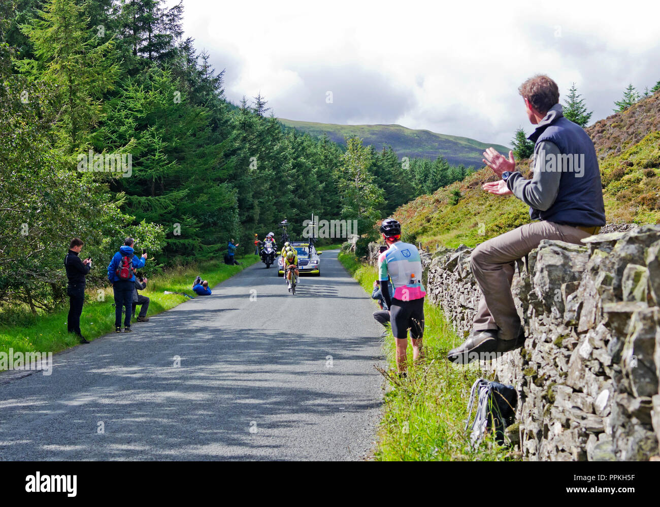 Stage 5 Tour of Britain 2018. Spectator sitting on dry stone wall applauds arrival of Michelton Scott in Team Time Trial, Whinlatter Pass, Cumbria. Stock Photo