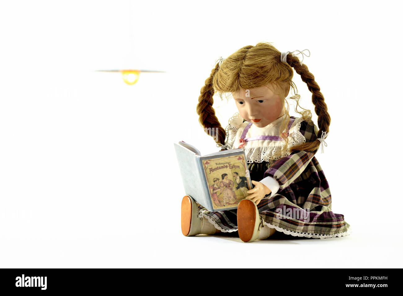doll Elise sits and is reading a book about decency (Germany). Puppe Elise liest ein Buch über Anstands-Lehre (Deutschland). Stock Photo