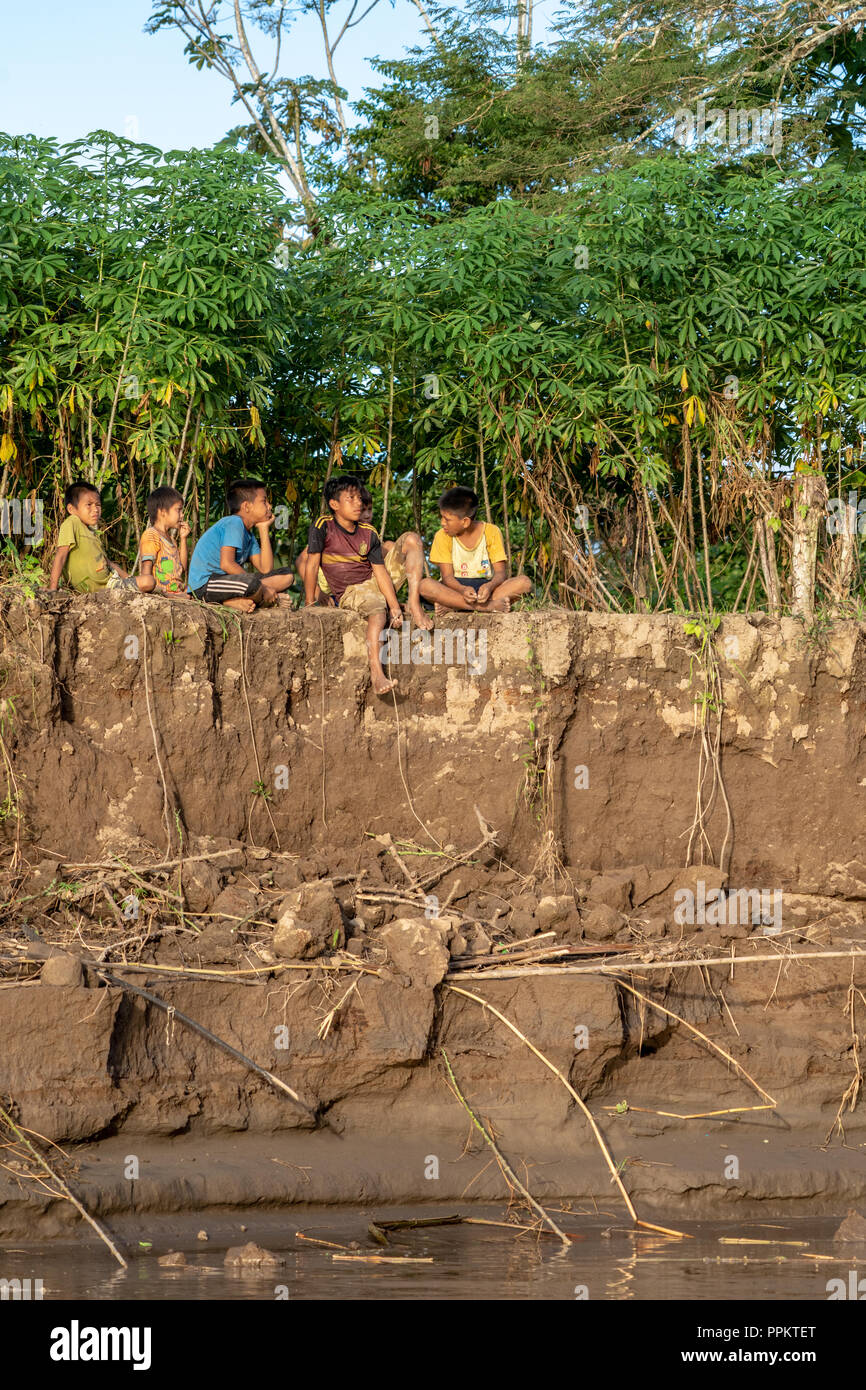 Nauta, Peru, South America.  Six bored young boys sitting on the steep riverbank of the Maranon river, an Amazon river tributary. Stock Photo