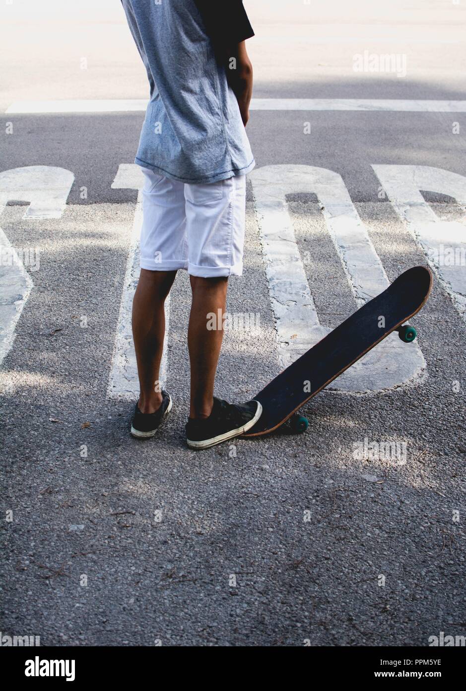 The boy with his skateboard staying on stop sign painted on asphalt road Stock Photo