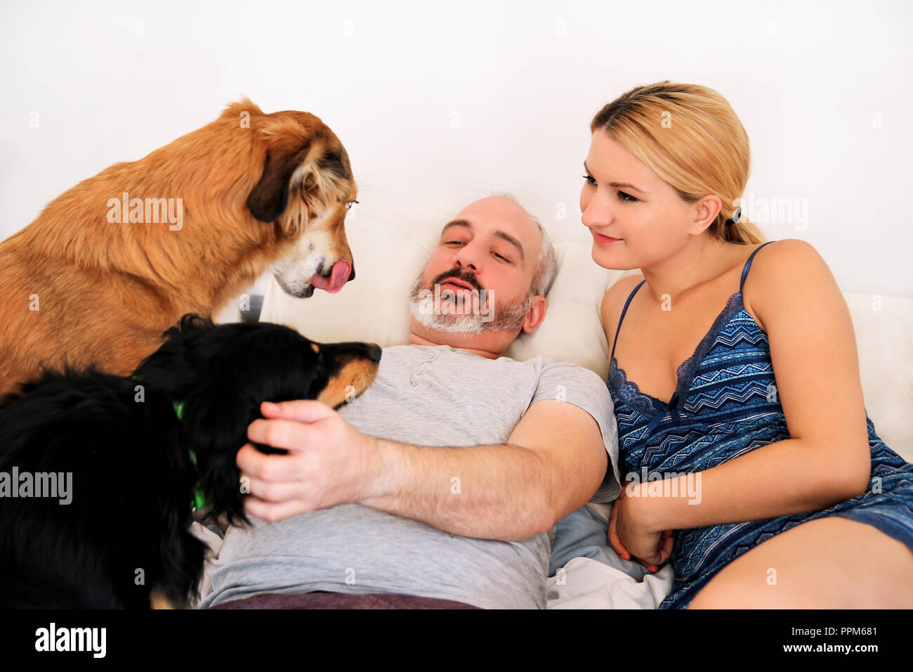 Handsome couple with their dogs on bed in morning. Young man and woman spending time with their pets in bedroom. Happiness couple enjoying. Stock Photo