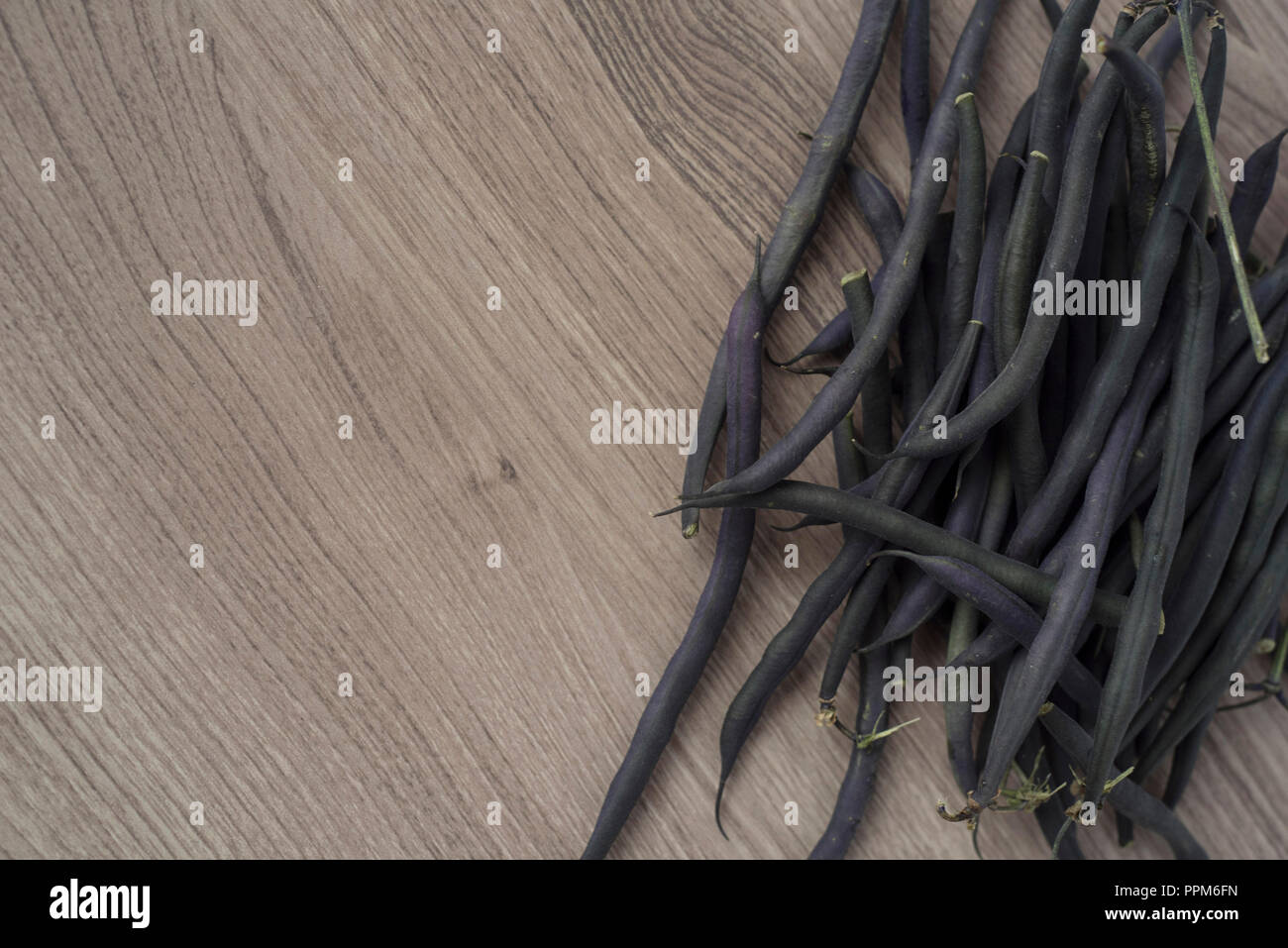 Purple Beans Piled in a Corner of a Light Wood Counter Overhead View Stock Photo