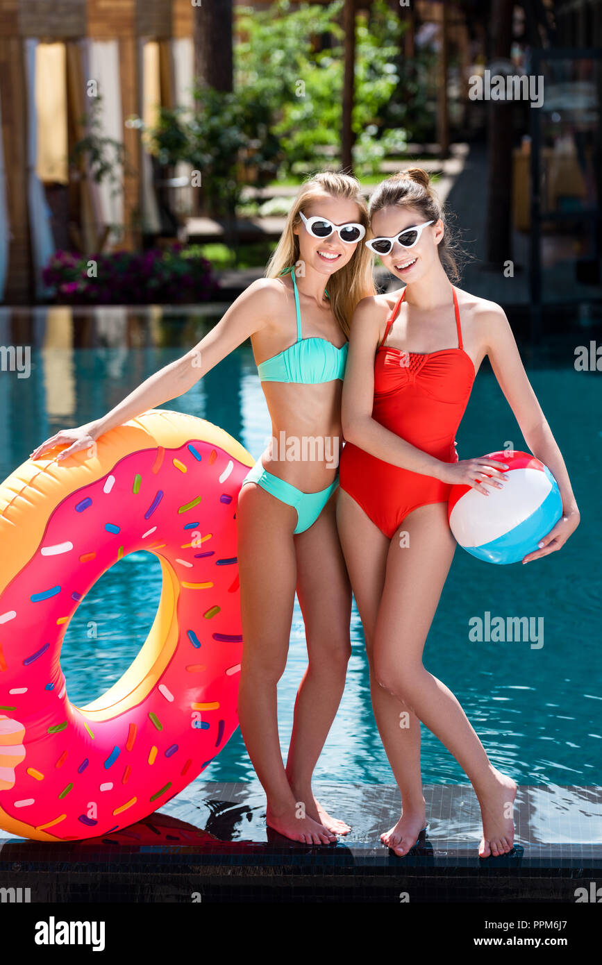 smiling young women with inflatable ring in shape of donut and beach ball  standing at poolside Stock Photo - Alamy