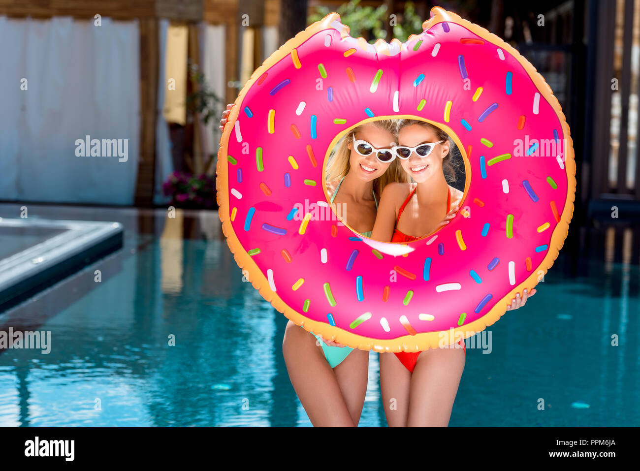 beautiful young women looking at camera through inflatable ring in shape of bitten donut at poolside Stock Photo