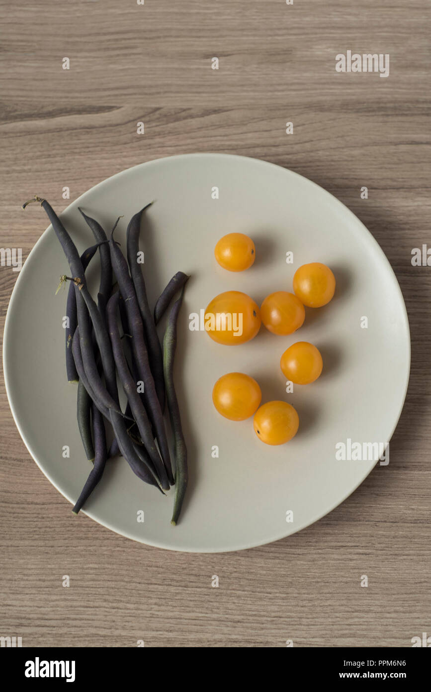 Overhead View of Purple Green Beans and Yellow Cherry Tomatoes on a Plate Stock Photo