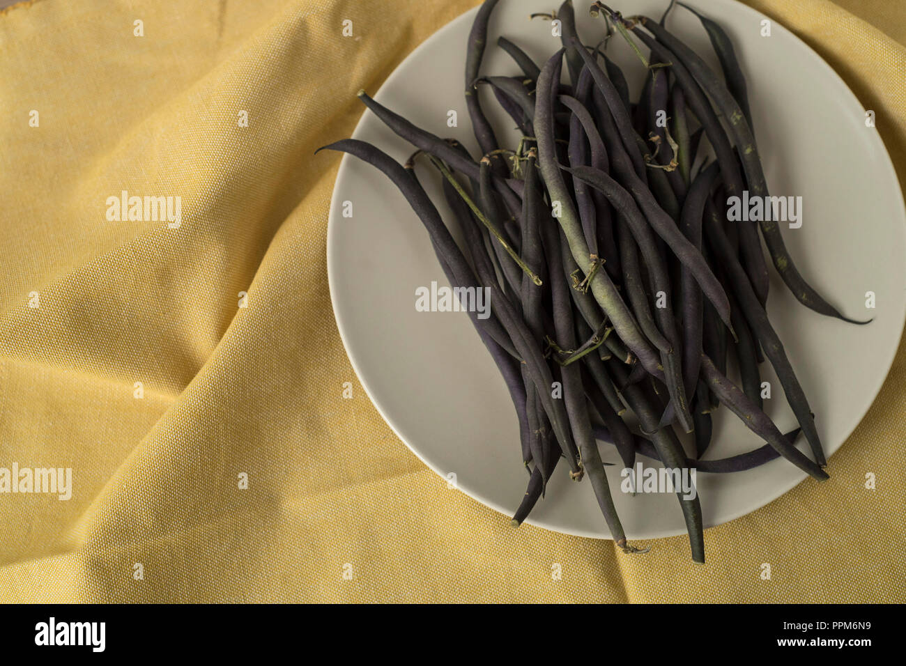 Purple Green Bean Pile on a Dish over Yellow Cloth Texture Stock Photo