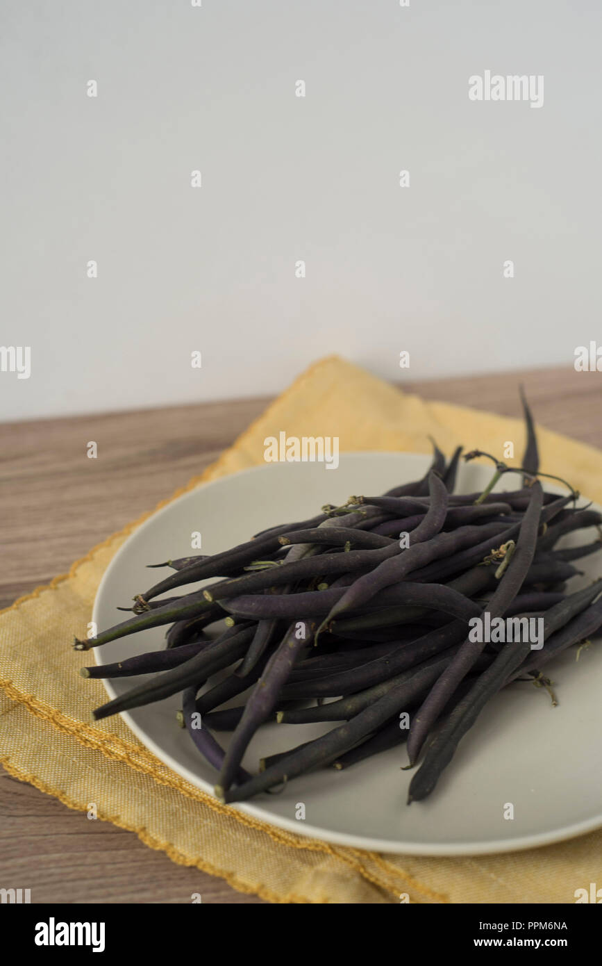 Loose Purple Green Beans on a Plate over a Yellow Napkin - Vertical View with Copy Space Stock Photo