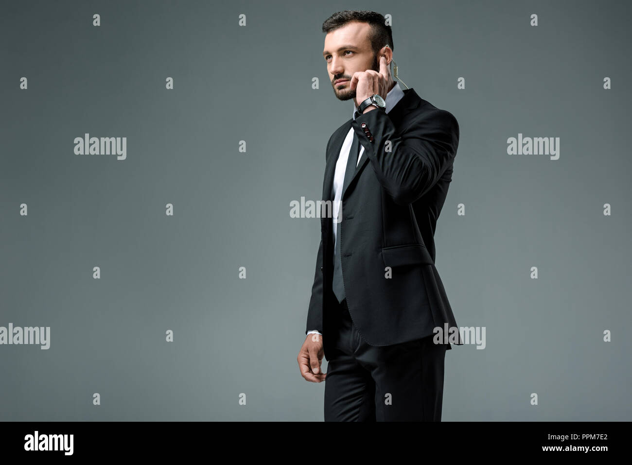 Handsome security guard listening message with security earpiece isolated on grey Stock Photo