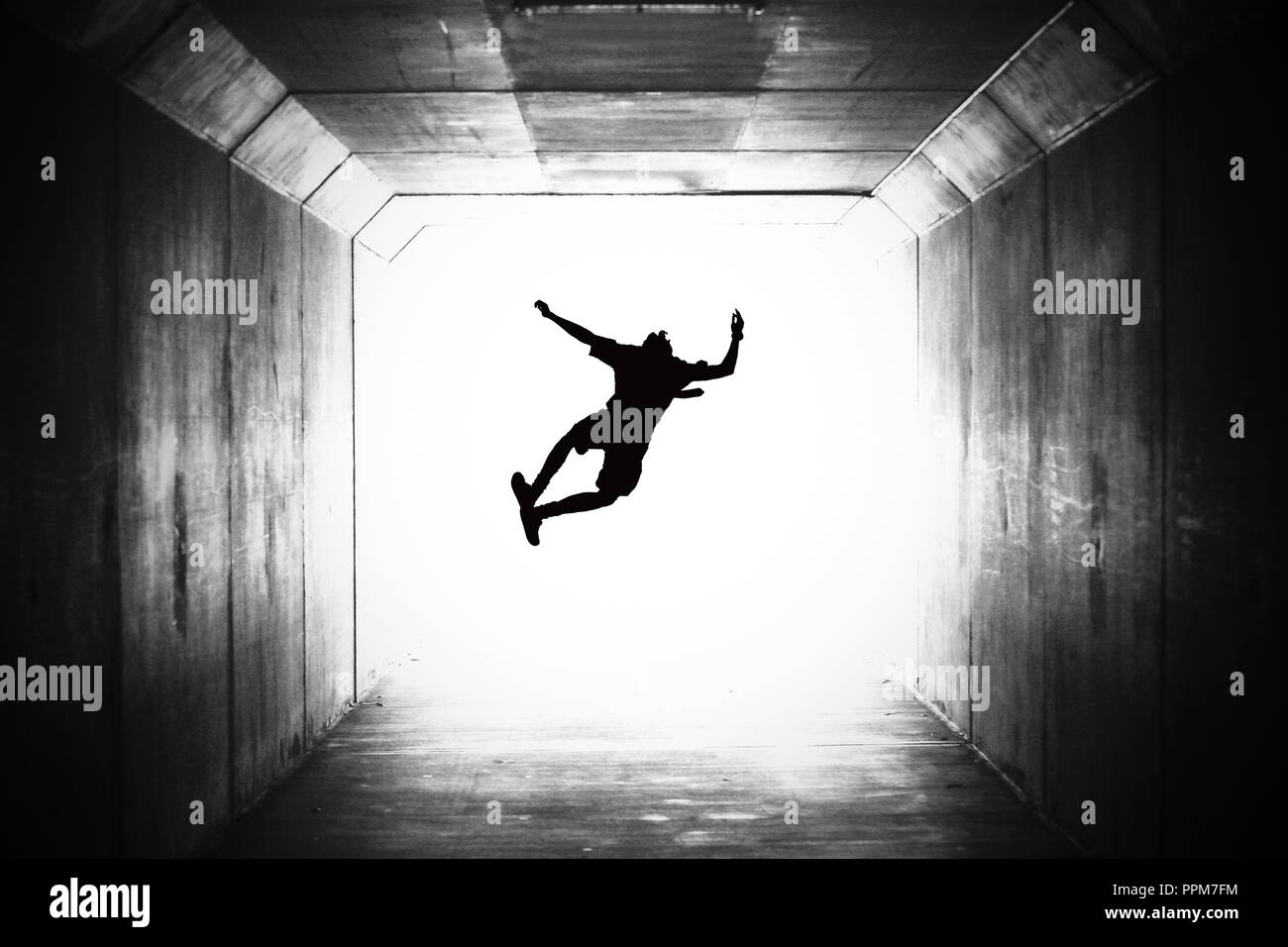 BW black and white image of a single school student silhouetted jumping up and clicking their heels in a tunnel. heading towards the light, graduation Stock Photo