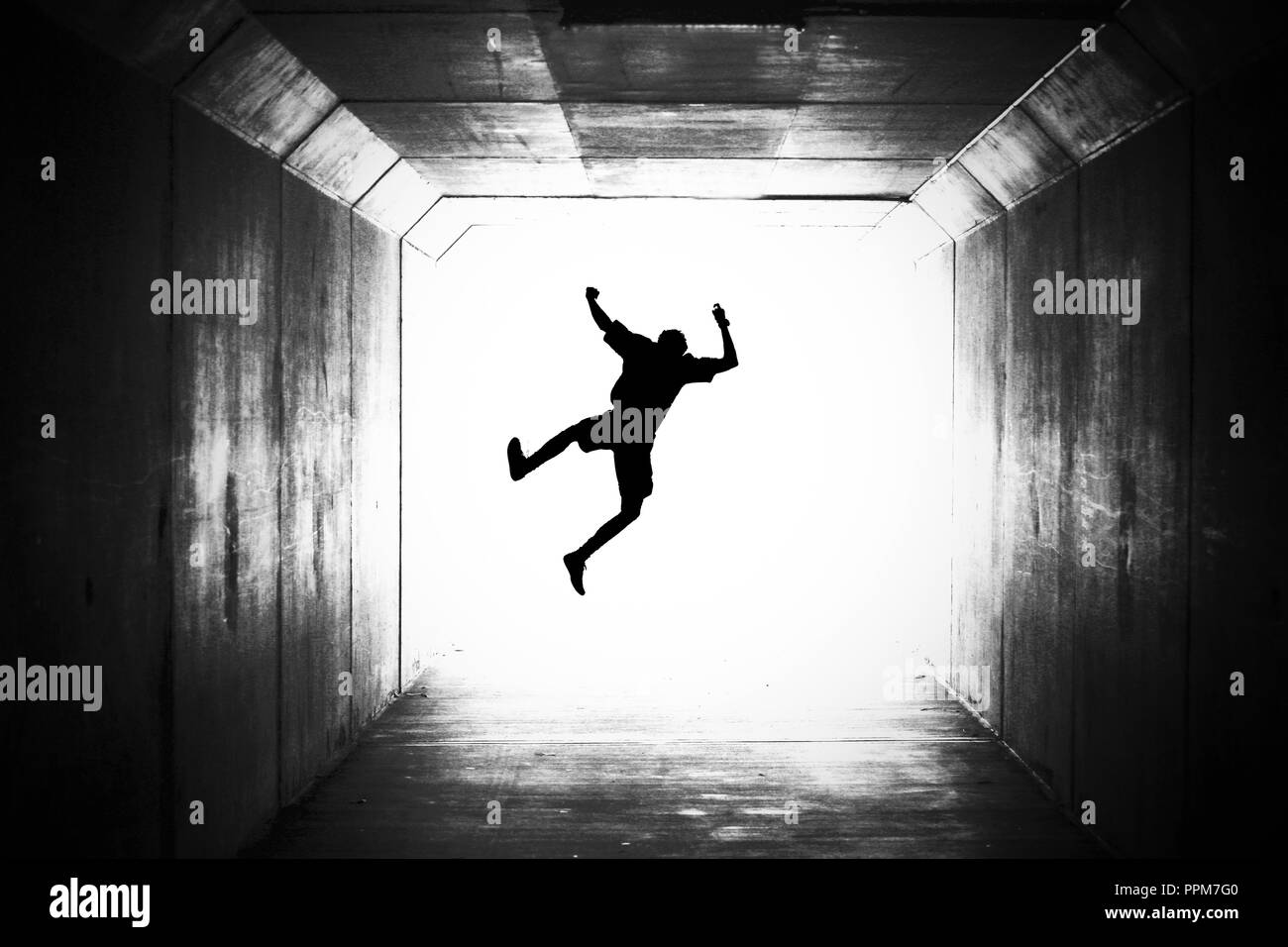 silhouette of a male figure jumping towards the light. graduation happy joy concept or death dying going out with a bang theme. crossing over, jumping Stock Photo