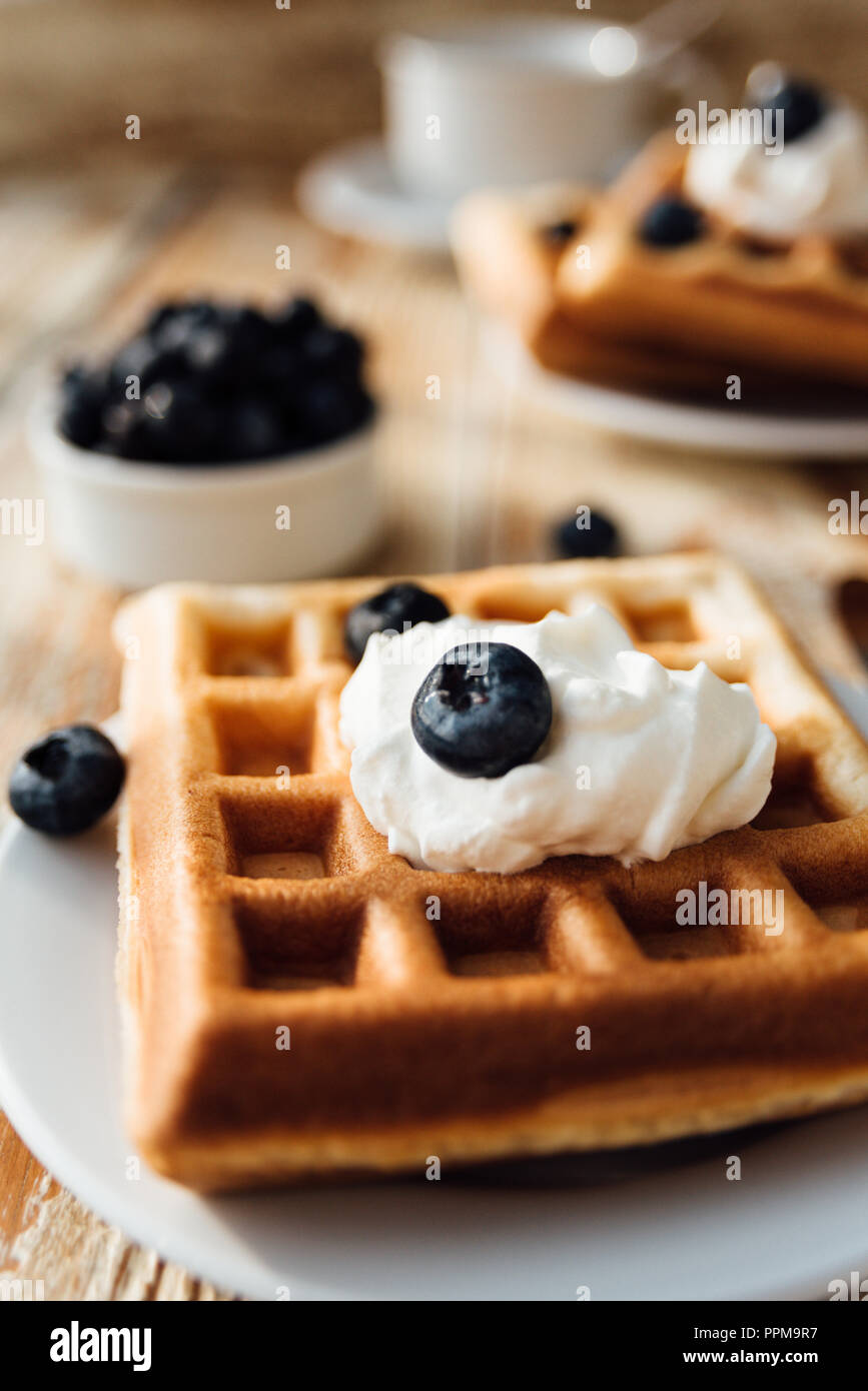 Brussels waffles with blueberry and whipped cream on wooden table at