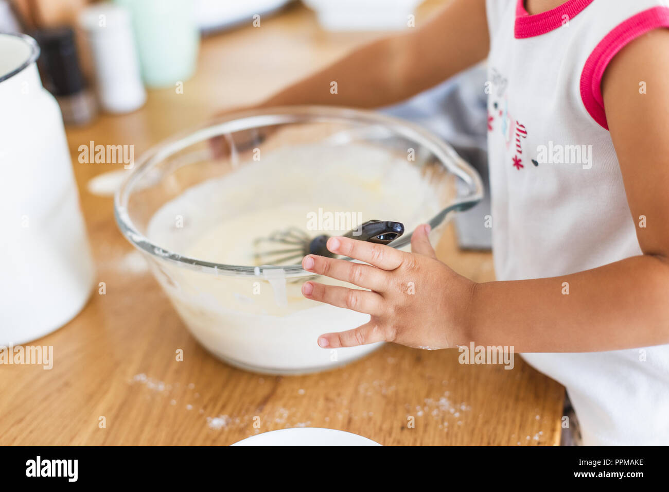 Little girl preparing dough for pancakes at the kitchen. Concept of food preparation, white kitchen on background. Casual lifestyle photo series in re Stock Photo