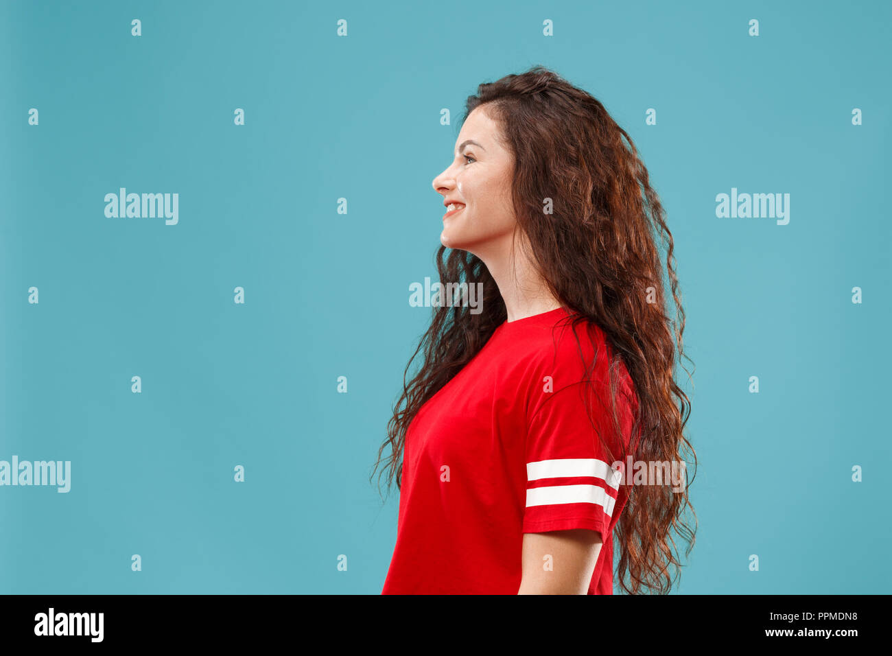 Happy business woman standing and smiling isolated on blue studio background. Beautiful female half-length portrait. Young emotional woman. The human emotions, facial expression concept. Profile view. Stock Photo