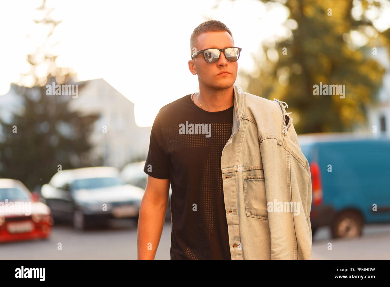 Fashionable man with stylish sunglasses in a black T-shirt and jeans jacket at sunset Stock Photo