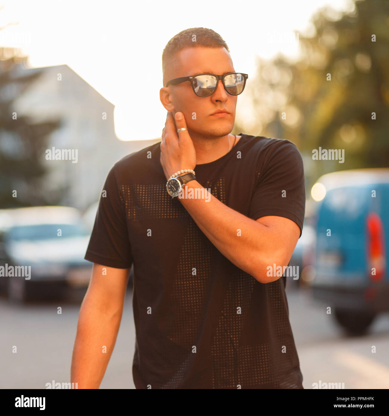 Hipster man with a hairdo in stylish sunglasses and a black fashion T-shirt at sunset Stock Photo