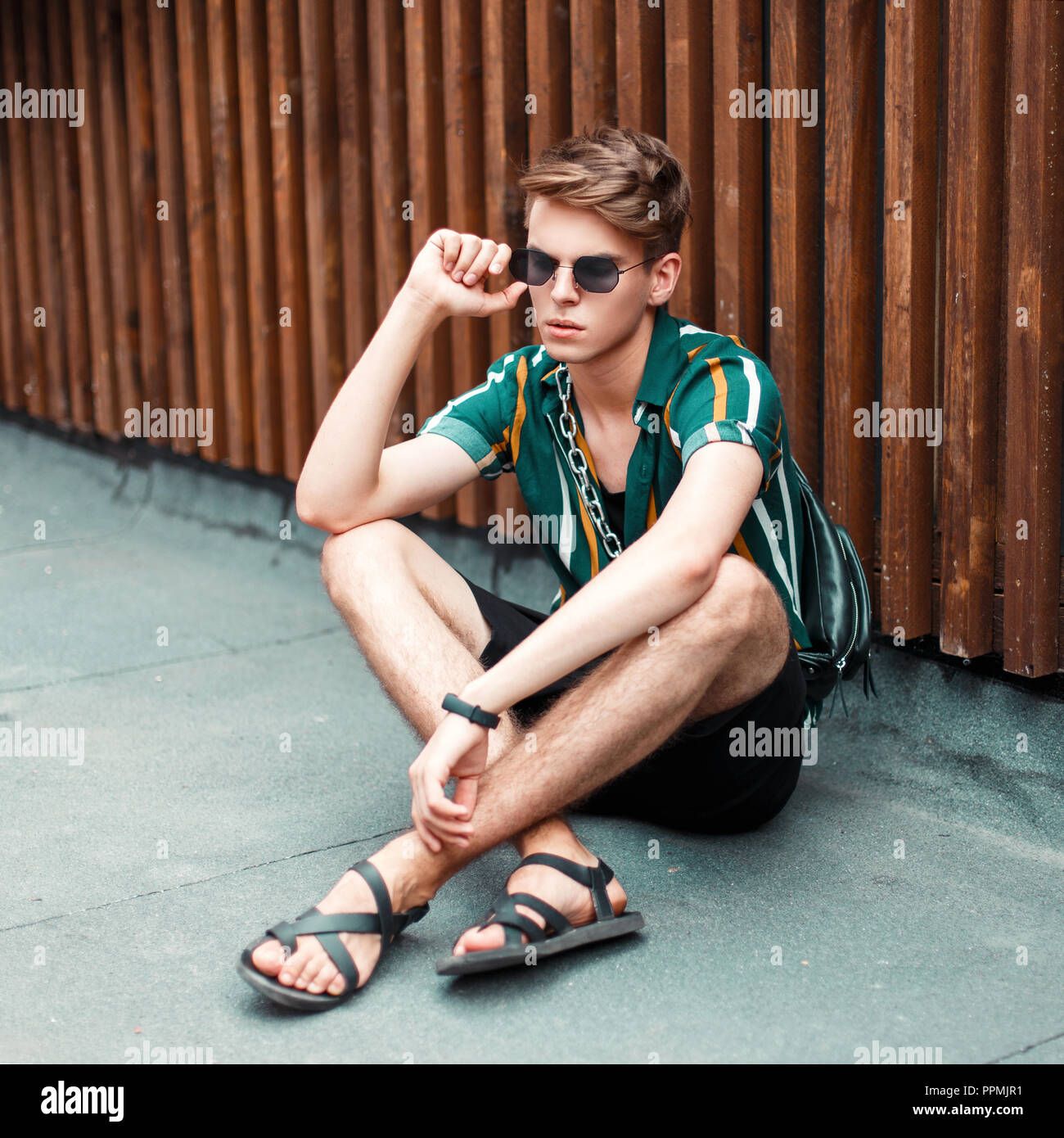 Handsome young stylish man with a hairstyle in fashion summer clothes  sitting on the street Stock Photo - Alamy