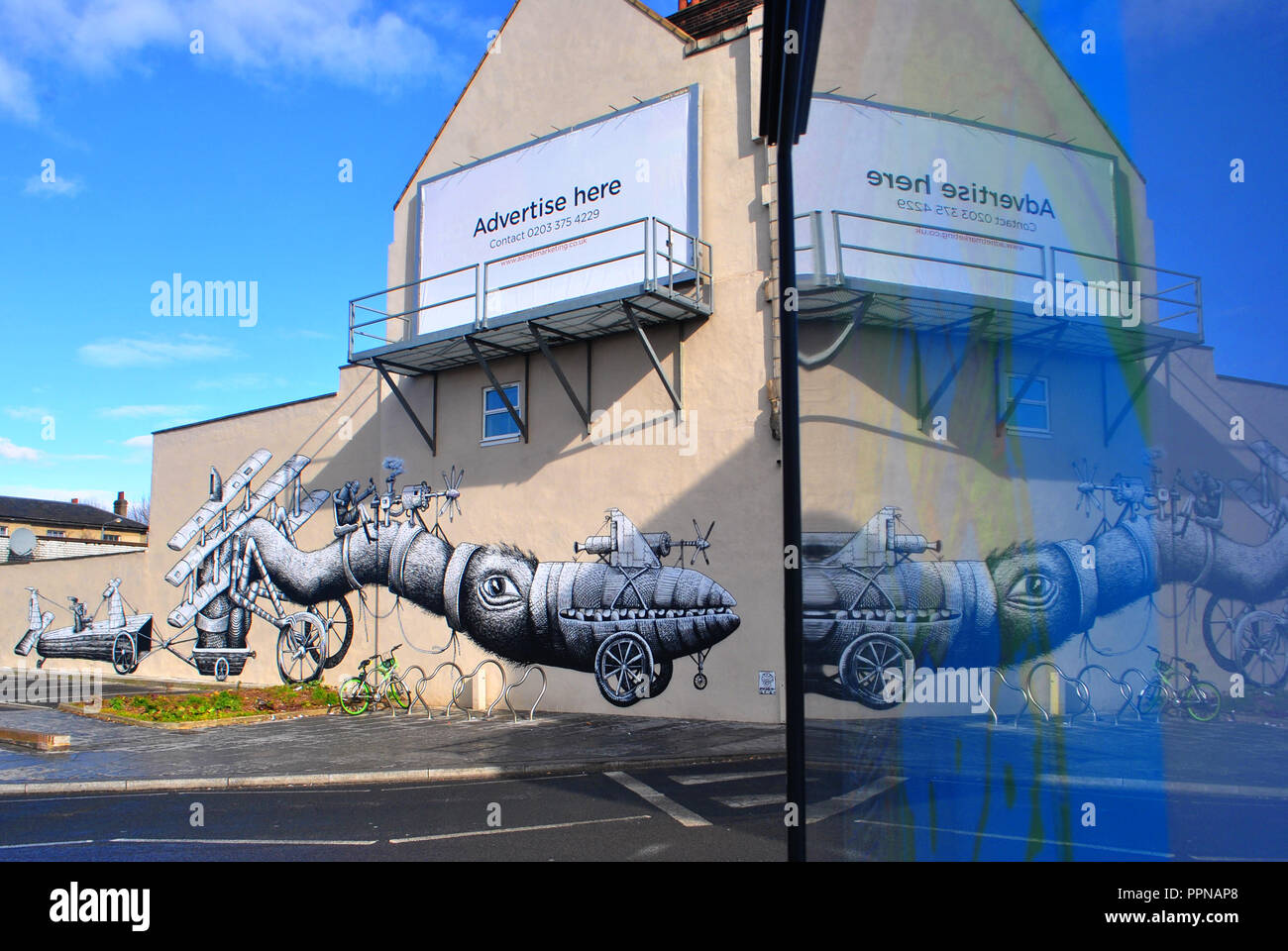 WEIRD,LARGE SCALE STREET ART BY ARTIST PHLEGM ON A WALTHAMSTOW WALL & PARTLY REFLECTED IN A ADVERTISING STAND. Stock Photo