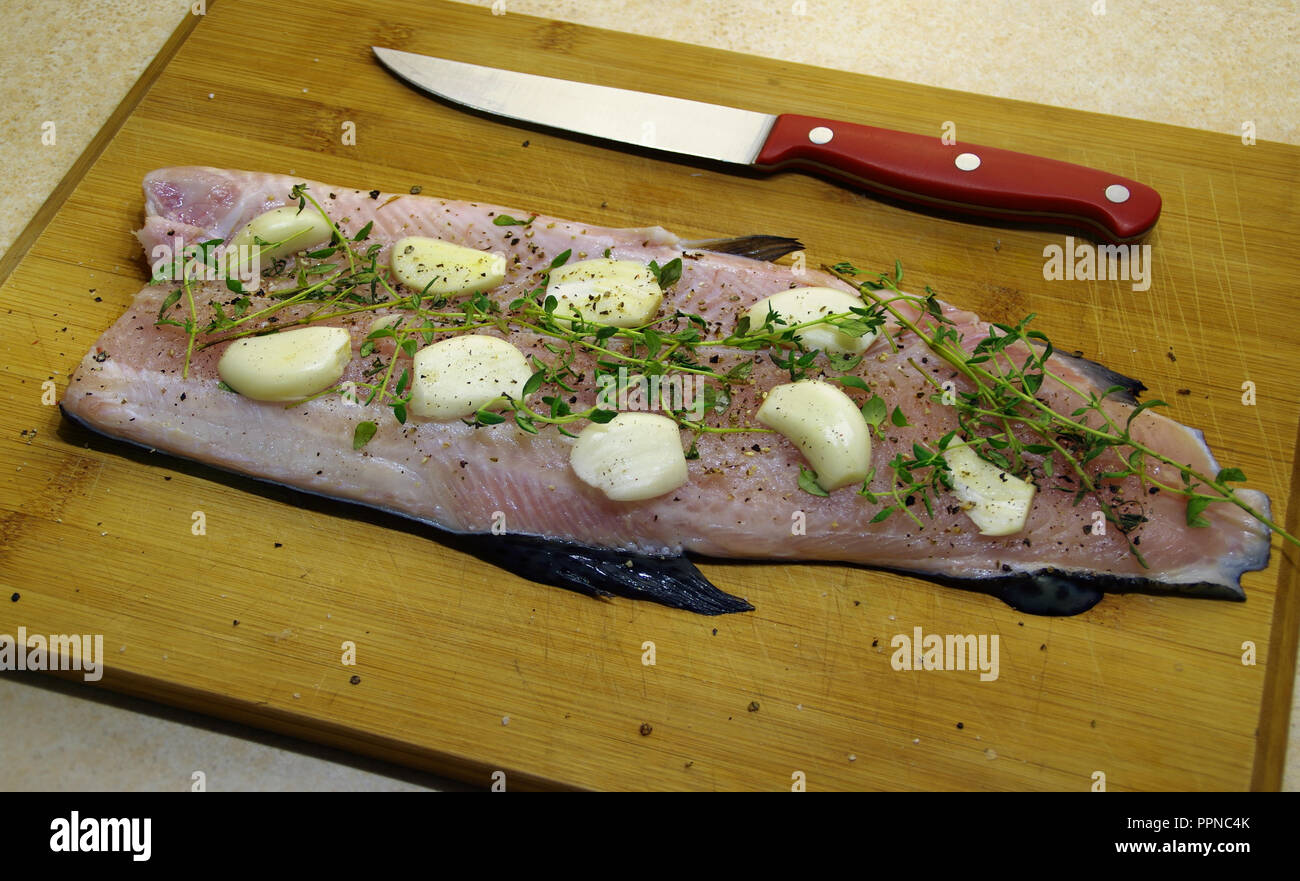 Trout fillet with herbs, garlic and spices on a wooden board. Fresh raw fish prepared for baking. Stock Photo