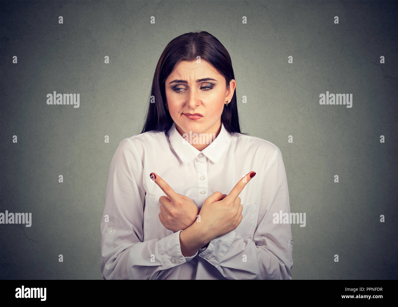 Young uncertain woman looking stressed while pointing with fingers in opposite directions on gray background Stock Photo