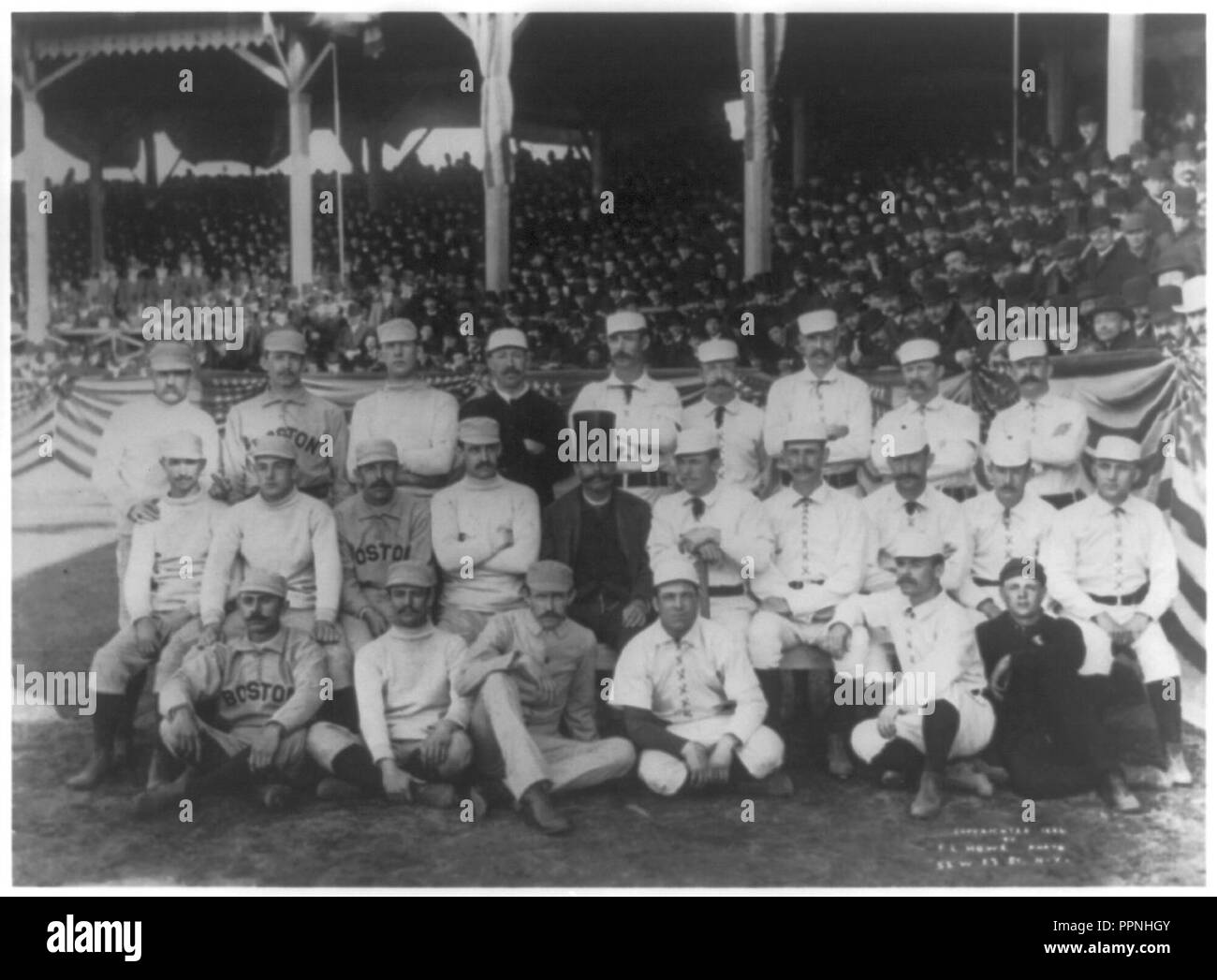 Boston and New York players on opening day, 1886, at the Polo Grounds, 5th Ave. & 110th St., N.Y.C. posed in front of stands; Boston player in back rowon left has his middle finger raised in Stock Photo