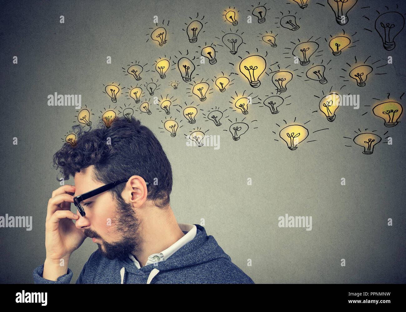 Young man thinking looking concentrated having many ideas with backdrop of bright lightbulbs. Stock Photo