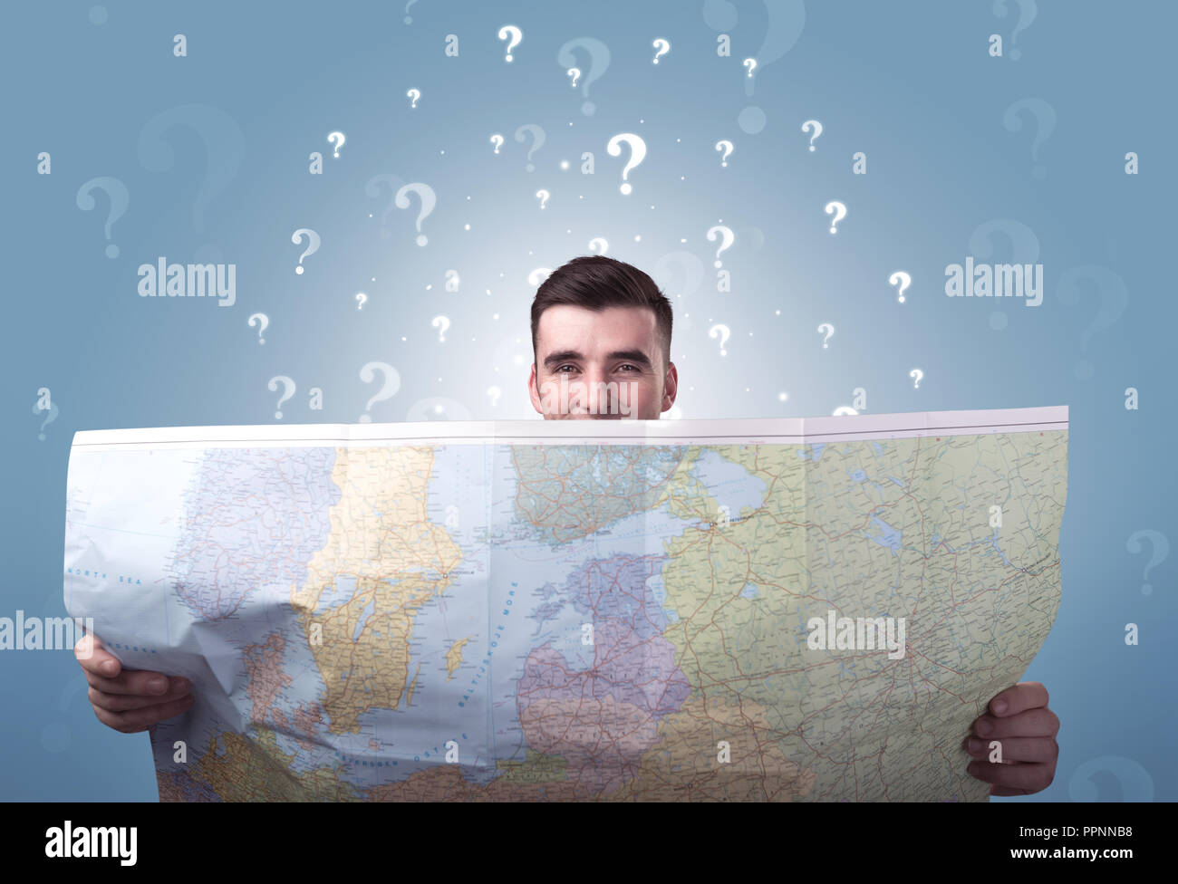 Handsome young man holding a map with white question marks above his ...
