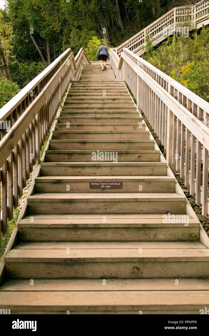 Woman climbing near top of a steep set of outdoor wooden stairs. Tourist climbing stairs leading to Arch Rock on Mackinac island, Michigan. Stock Photo