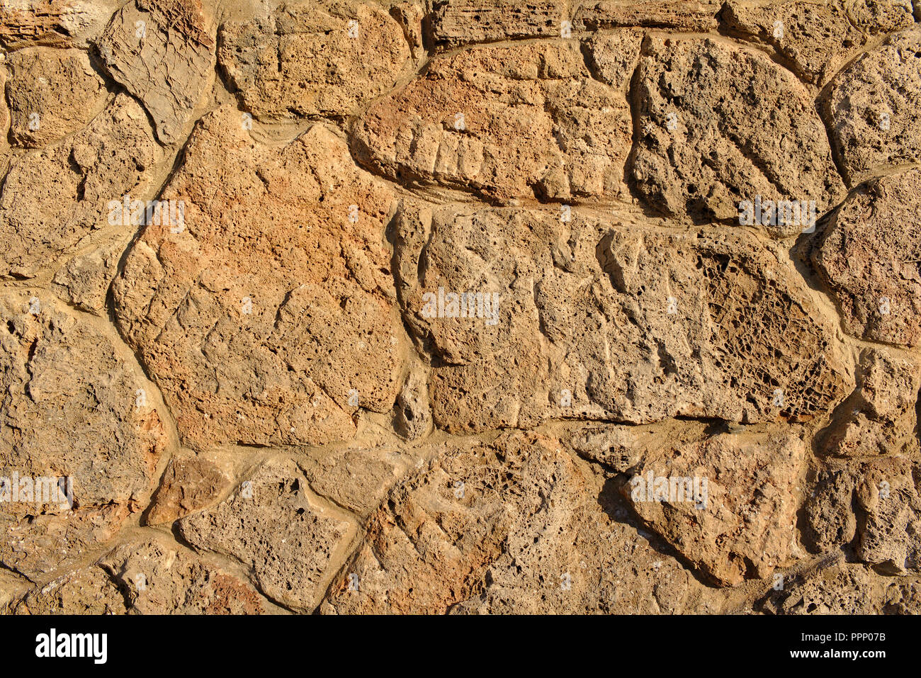 Sandstone wall made of irregular porous pieces of stone lit by the evening sun Stock Photo
