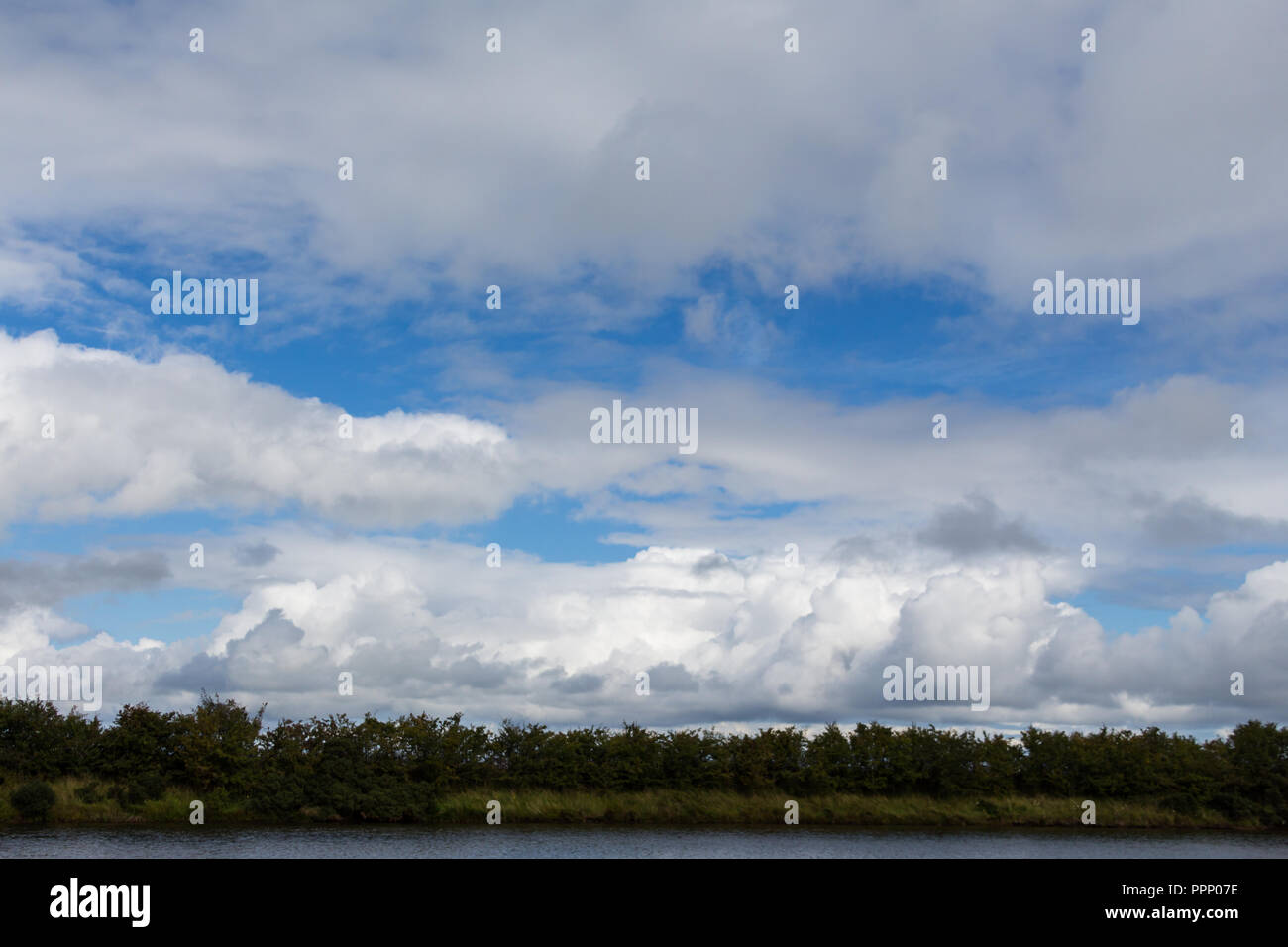 Blue sky and white clouds in lovely skyscape over trees and water Stock Photo