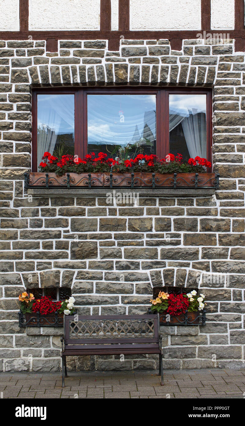 Wooden bench in front of old gray stone wall with two small windows ...