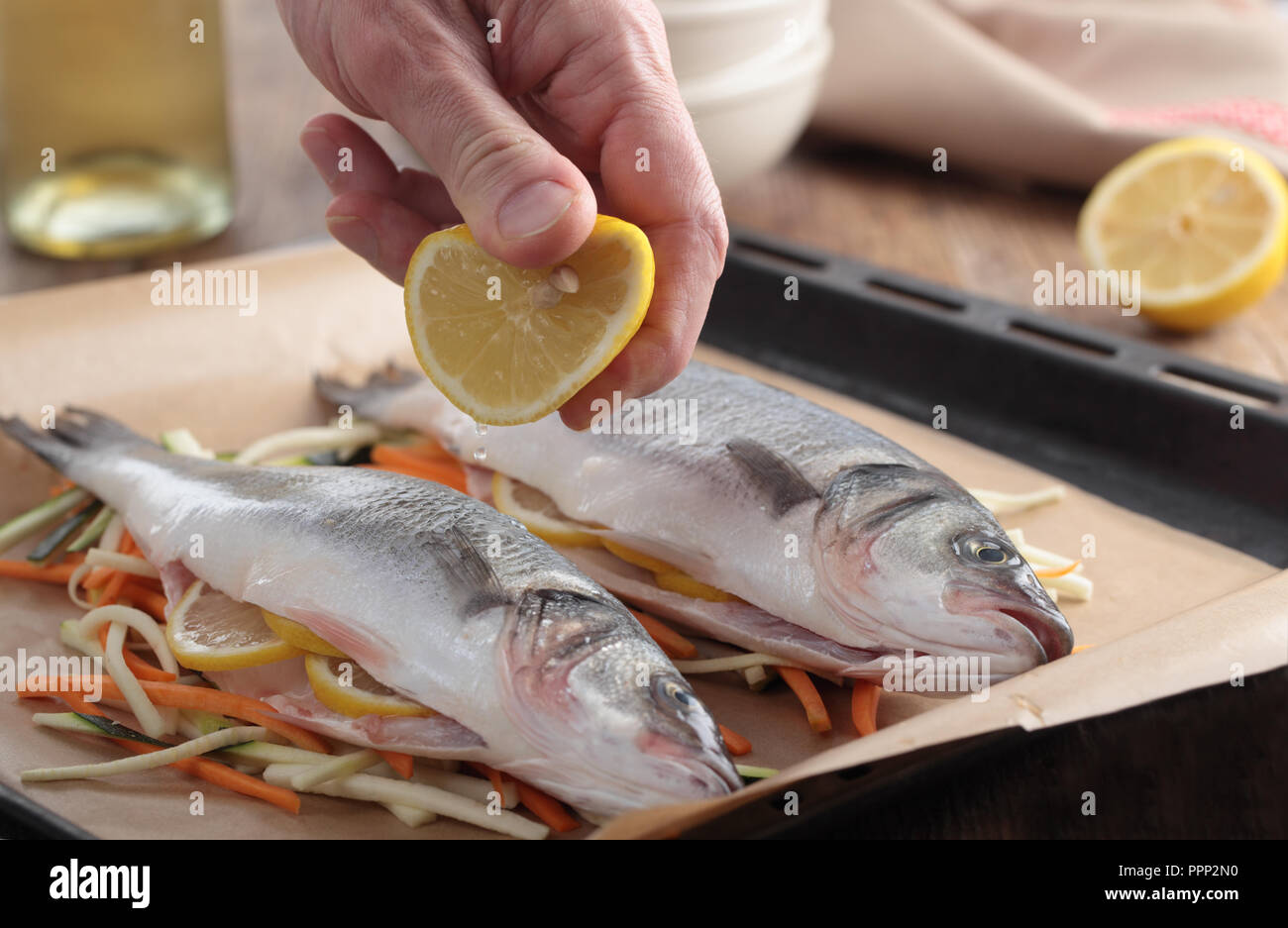 Squeezing the lemon onto raw sea basses on a bed of vegetables before  baking Stock Photo - Alamy